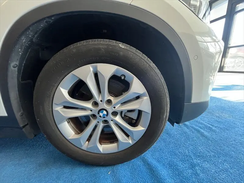 Gros plan sur la roue avant gauche d'un BMW X1 XDRIVE blanc alpin, mettant en valeur la jante alliage et le logo BMW.