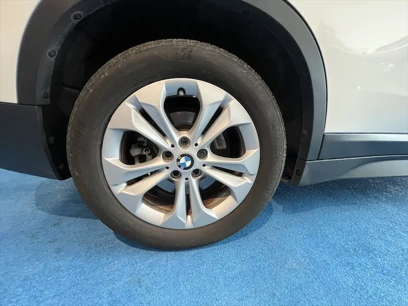 Gros plan sur la roue avant gauche d'un BMW X1 blanc alpin, mettant en valeur la jante alu et le logo BMW central.