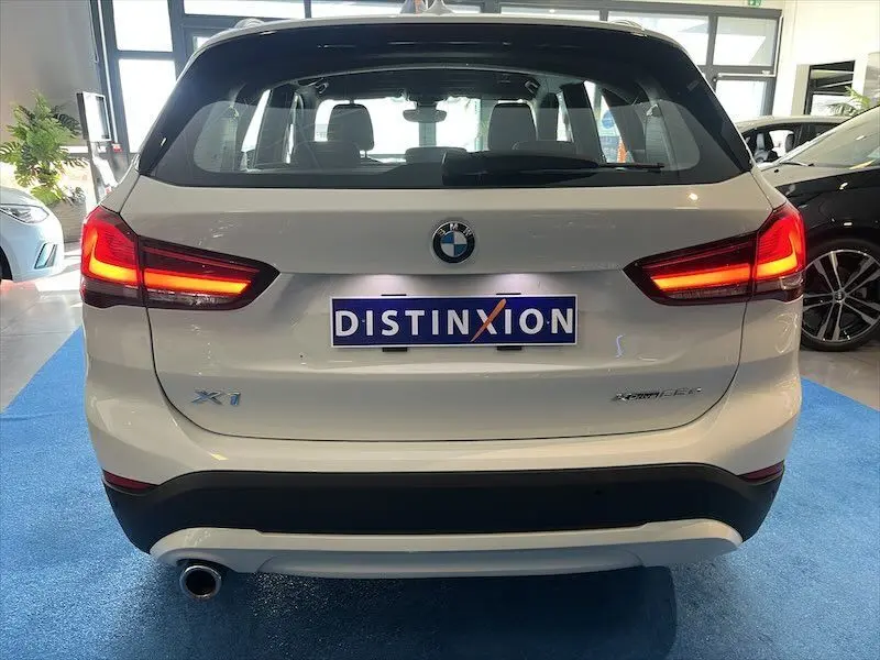 Vue arrière d'un BMW X1 XDRIVE blanc alpin avec feux allumés et plaque Distinxion en concession.