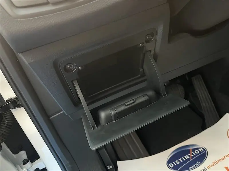 Ouverture du cendrier côté gauche intérieur d'un BMW X1 XDRIVE blanc alpin, avec pédales visibles en arrière-plan.