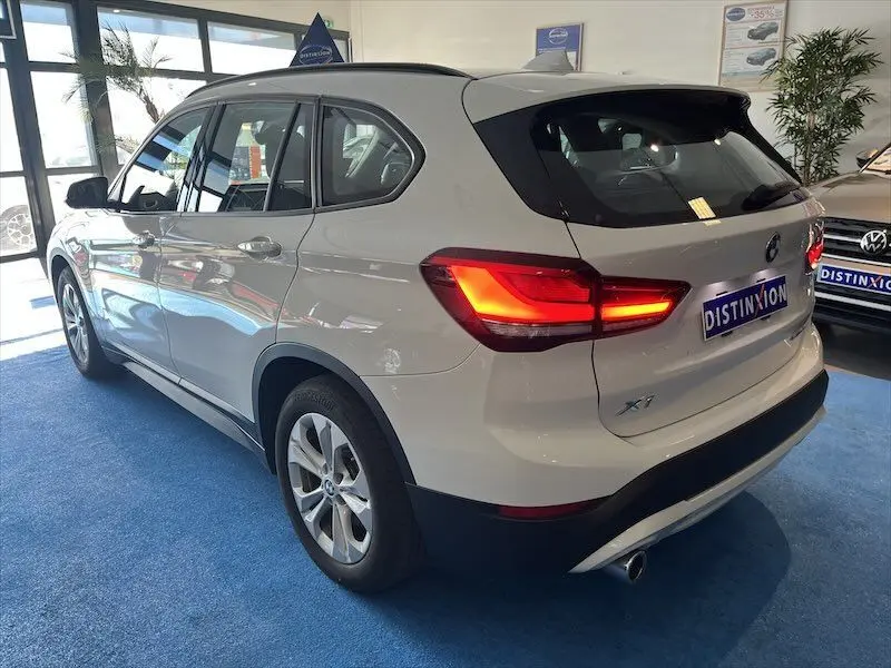 BMW X1 XDRIVE blanc alpin vu en 3/4 arrière droit avec feux arrière allumés dans un showroom.