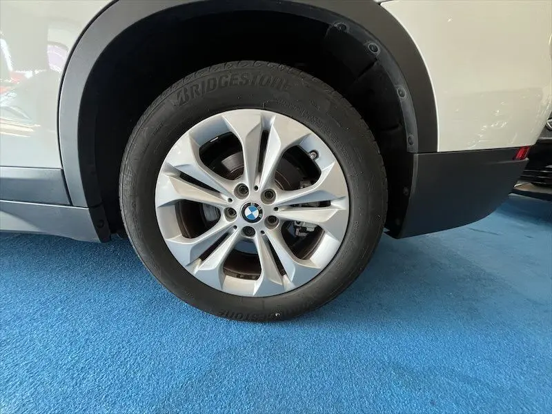 Gros plan sur la roue arrière droite d’un BMW X1 blanc alpin, mettant en valeur la jante argentée et le logo BMW central.