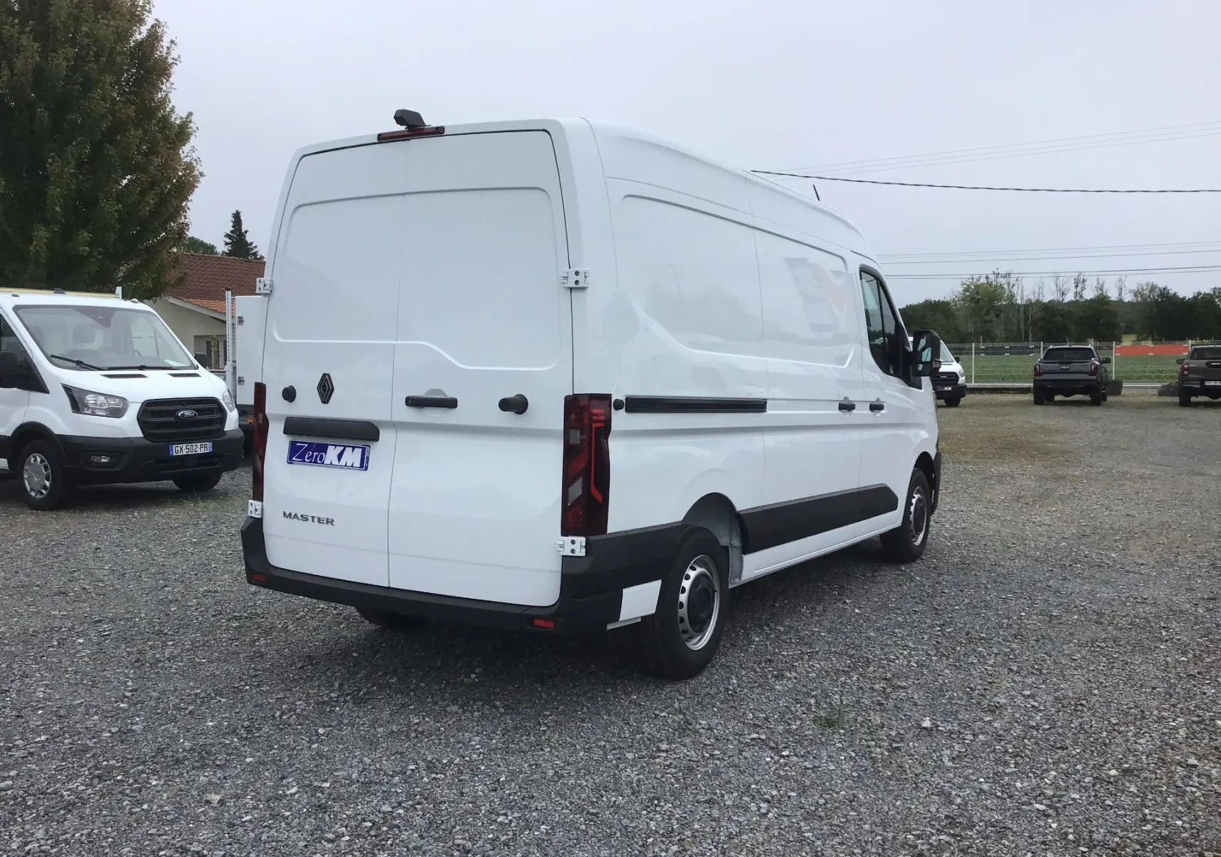 Vue 3/4 arrière droite d'un utilitaire Renault Master blanc L2H2 avec portes arrière fermées sur un parking.