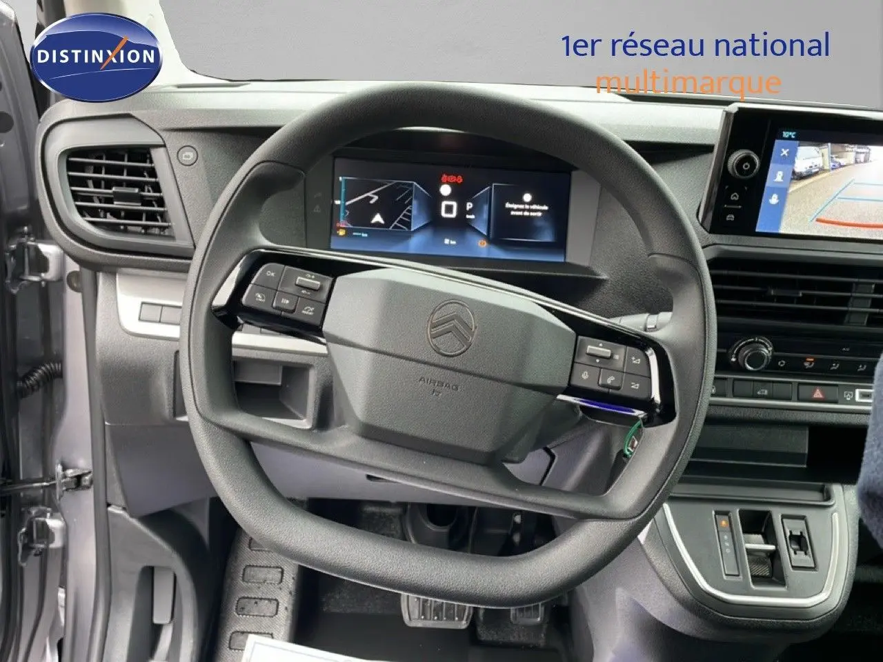 Vue intérieure centrée sur le volant du Citroën Jumpy gris, avec tableau de bord digital et écran de caméra de recul.
