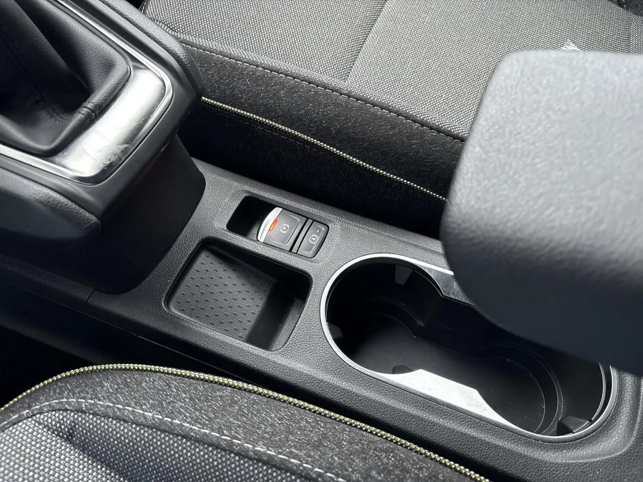 Gros plan sur la console centrale noire du Renault Captur 2025, avec frein à main électrique et accoudoir tissu.