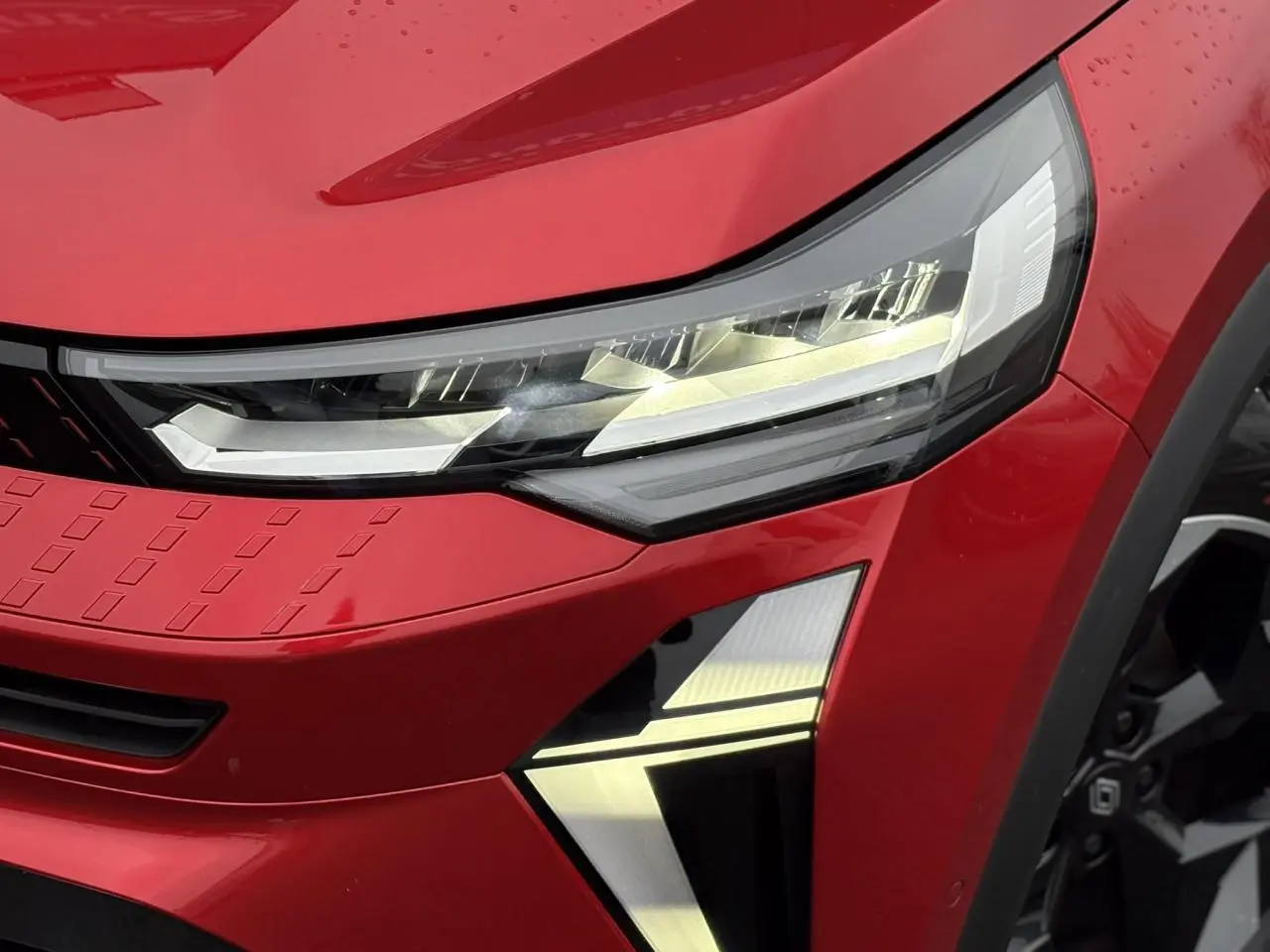Gros plan sur le phare avant droit du Renault Captur 2025 Rouge Flamme avec détails LED et jante alu noire visible.