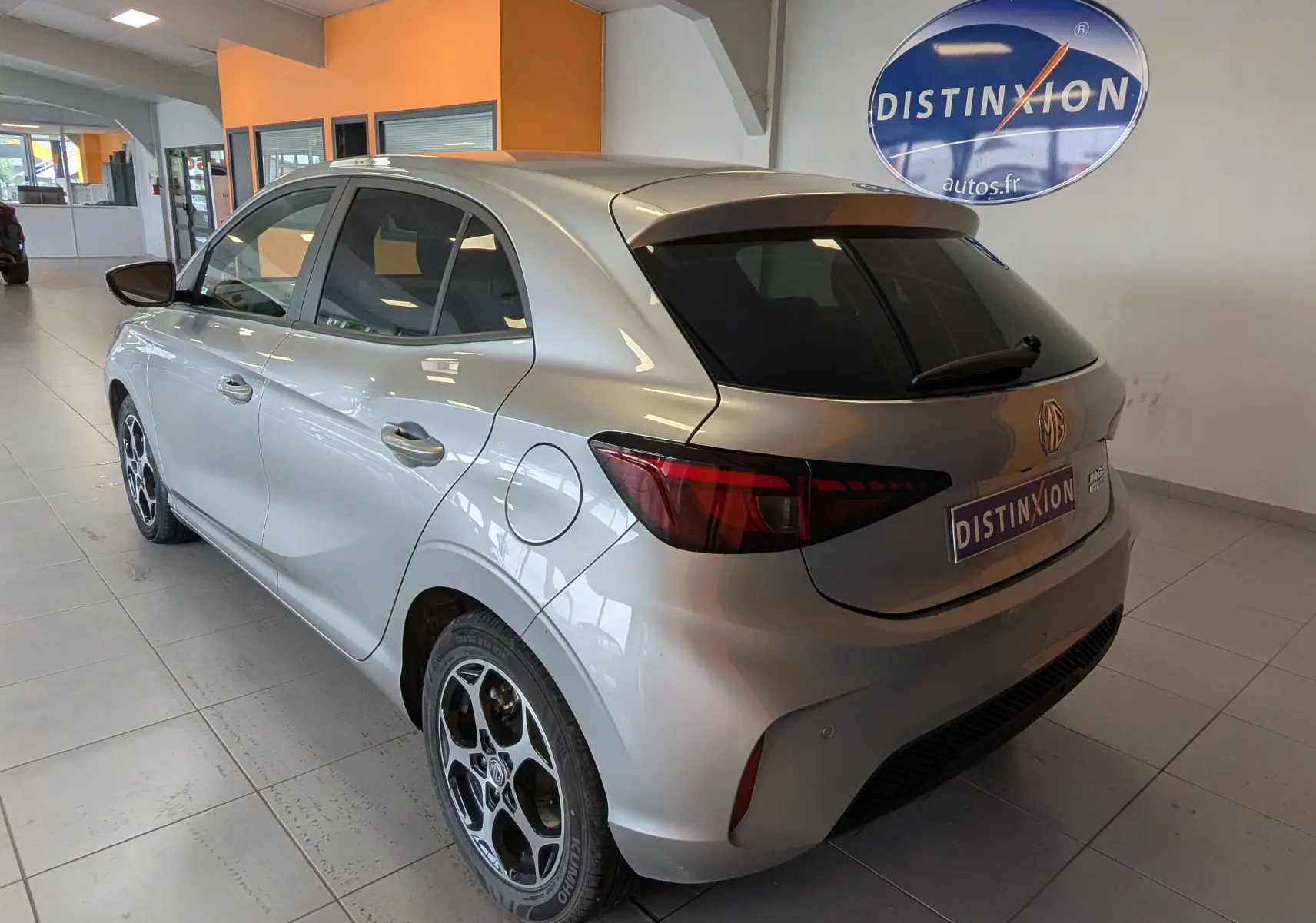 Vue 3/4 arrière droite de la MG3 1.5 L Hybrid+ cosmic silver avec jantes alliage 16 pouces et vitres teintées en intérieur showroom.