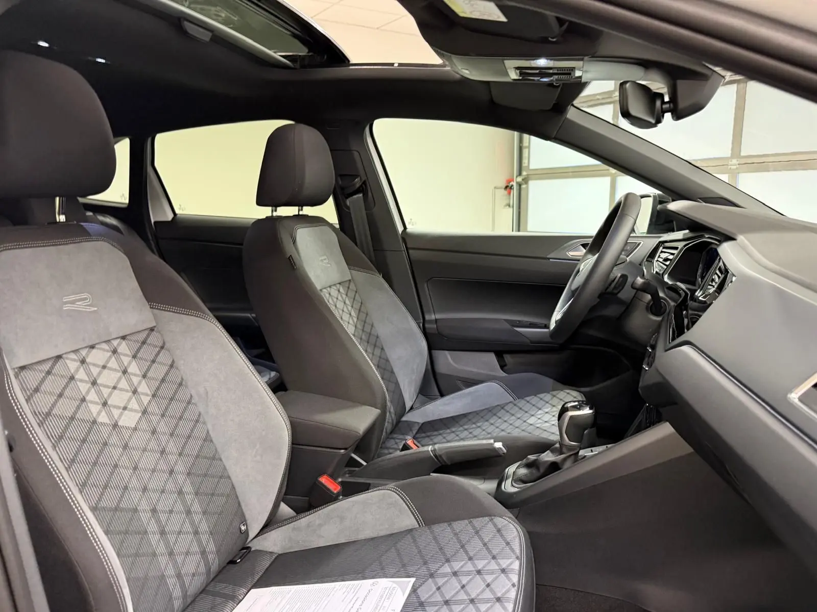 Vue intérieure côté conducteur du Volkswagen Taigo R-Line 2025, sièges sport gris avec surpiqûres et toit ouvrant noir visible.
