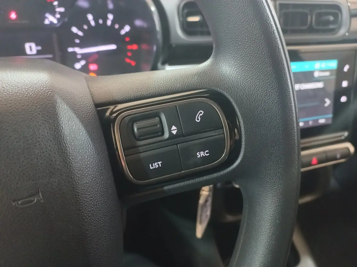 Gros plan sur le volant multifonctions noir de la Citroën C3 2024 avec commandes audio et écran tactile en arrière-plan.