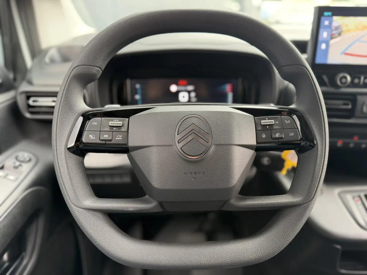 Vue rapprochée du volant multifonctions noir du Citroën Berlingo 2026 avec tableau de bord numérique en arrière-plan.