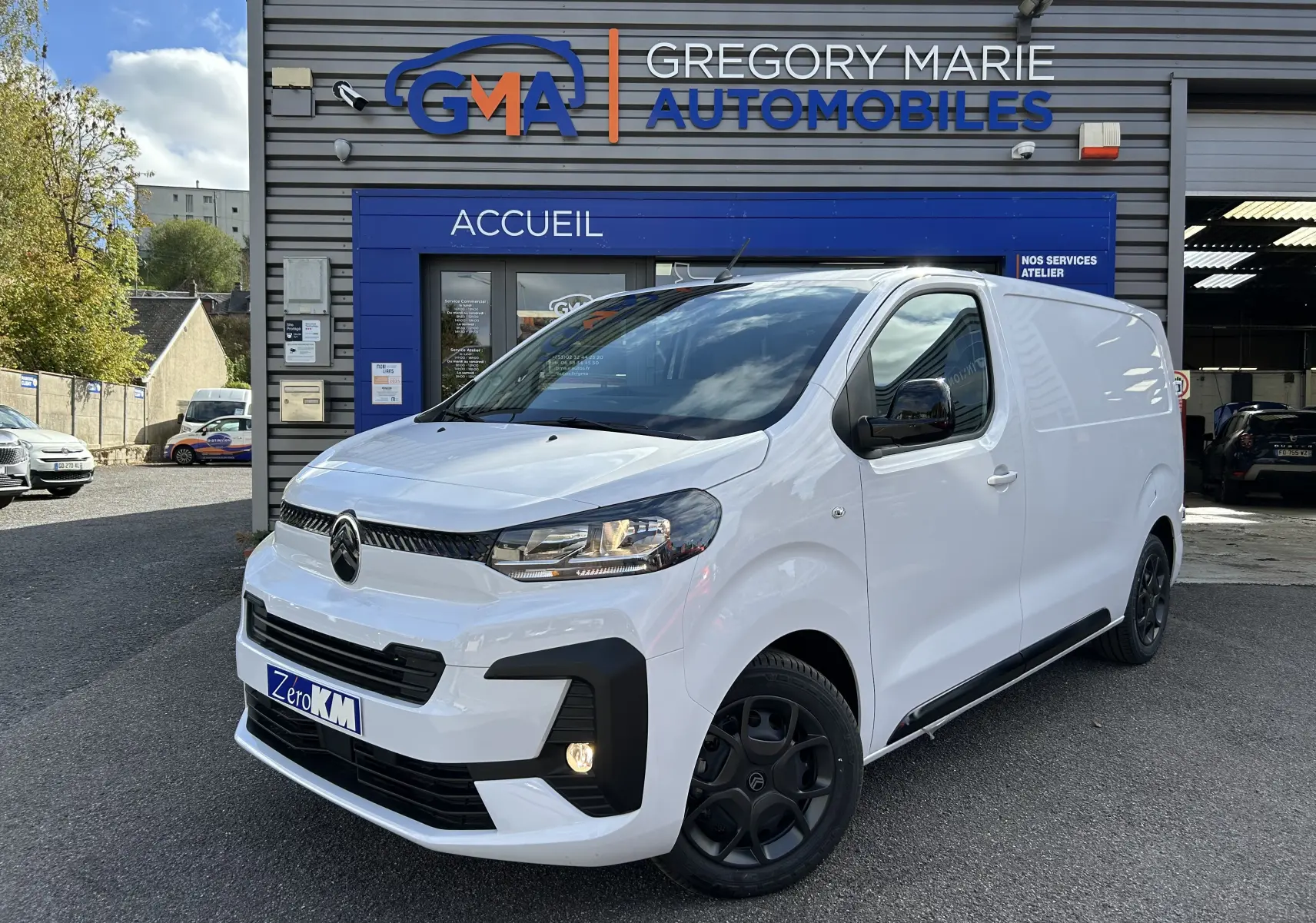 Fourgon Citroën Jumpy blanc en 3/4 avant droit, avec jantes noires et calandre moderne, devant un garage automobile.
