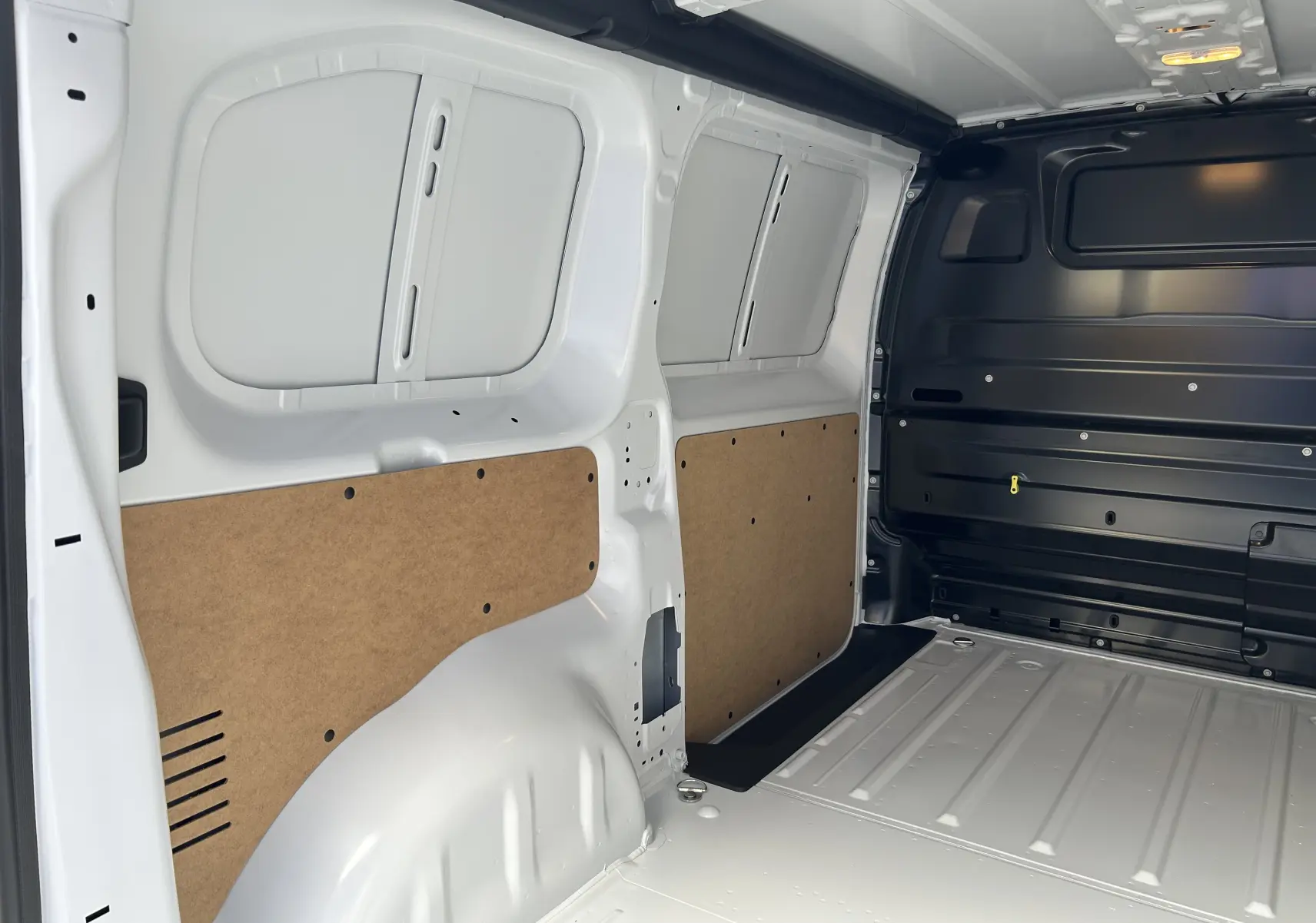 Intérieur du fourgon Citroën Jumpy blanc, vue latérale droite montrant la paroi et le plancher métalliques avec panneaux en bois.