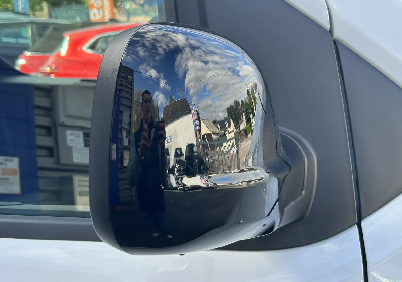 Rétroviseur côté droit brillant du Citroën Jumpy Fourgon blanc, reflétant un ciel nuageux et un environnement urbain.