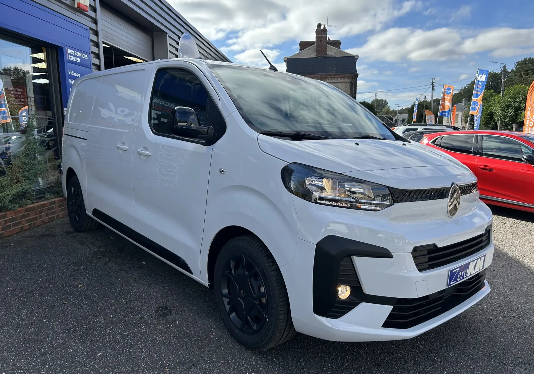 Fourgon Citroën Jumpy blanc en 3/4 avant droit, avec jantes noires et calandre moderne, stationné devant un atelier.