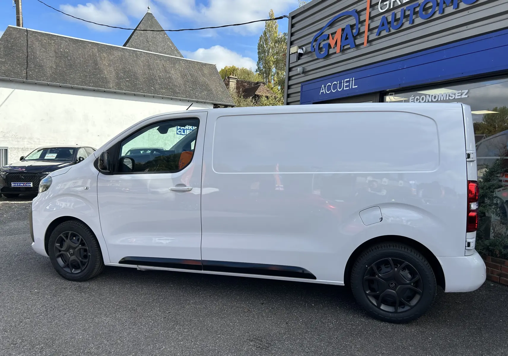 Vue de profil côté gauche d'un Citroën Jumpy Fourgon blanc 2025 avec jantes noires, stationné devant un bâtiment.