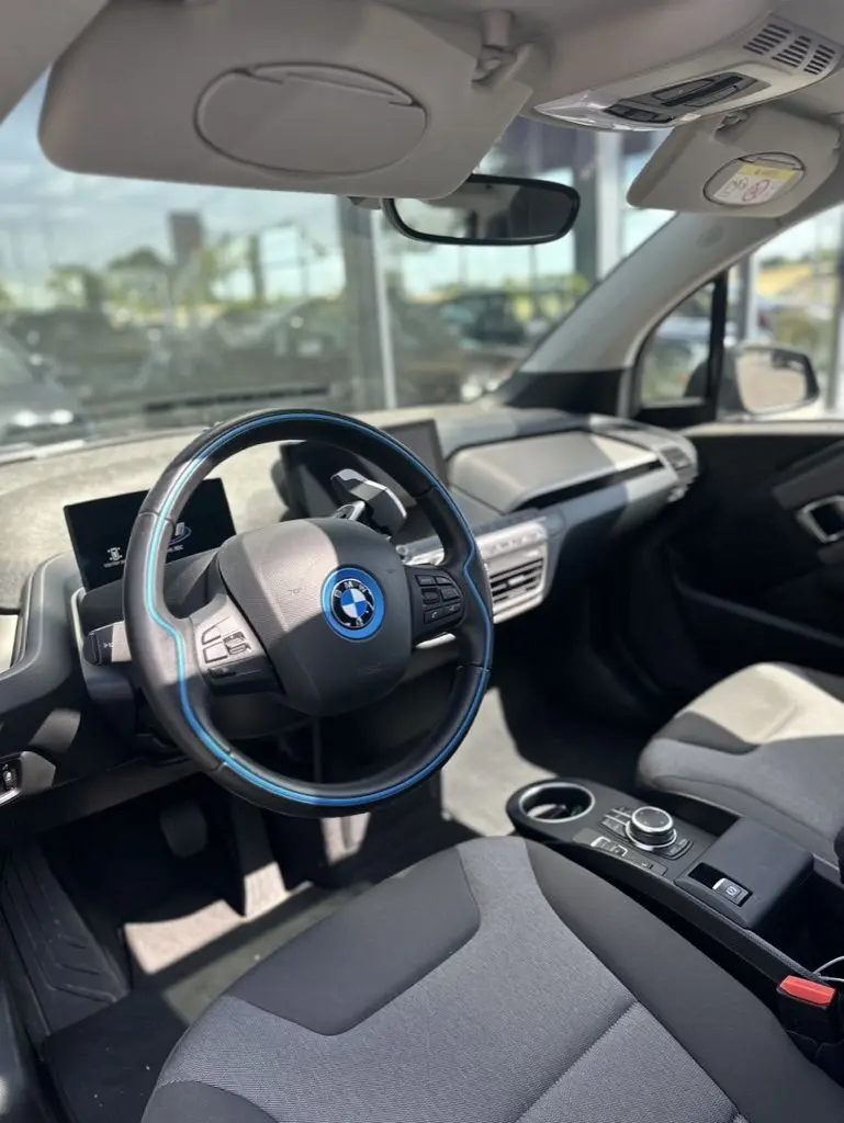 Vue intérieure côté conducteur de la BMW i3 noire 2022, volant avec liseré bleu et tableau de bord moderne.