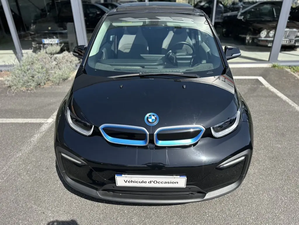 Vue avant plongeante d'une BMW i3 noire électrique avec calandre bleutée et plaque "Véhicule d'Occasion" visible.