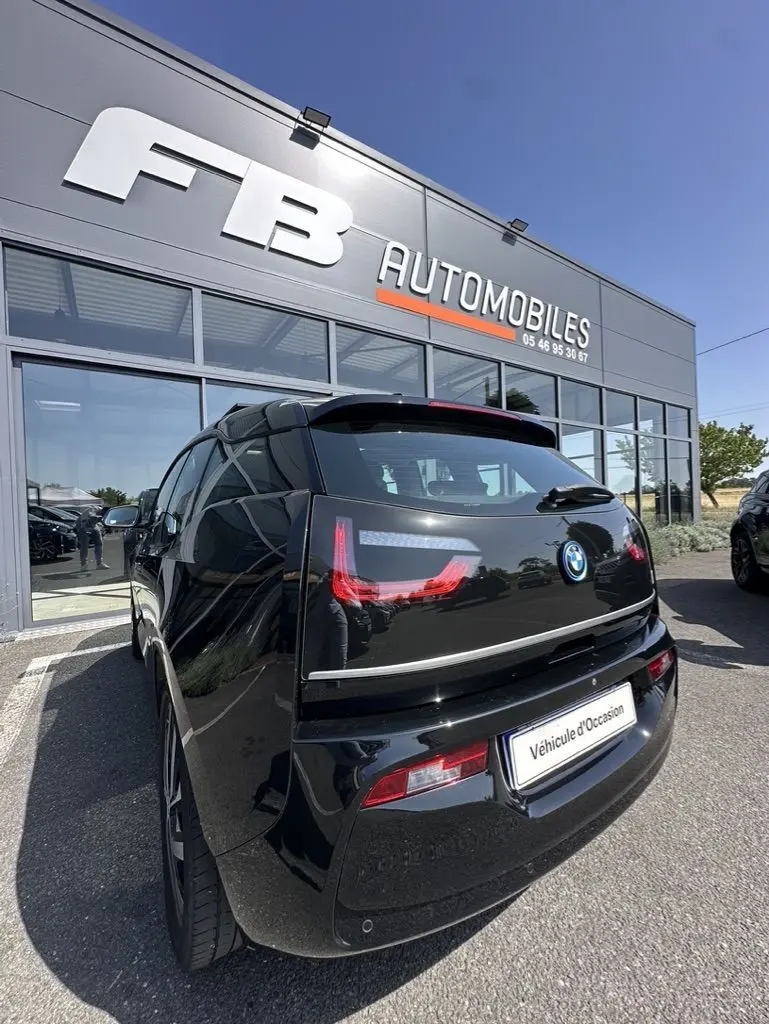 Vue 3/4 arrière d'une BMW I3 noire électrique 2022, avec feux arrière LED distinctifs, stationnée devant un concessionnaire.