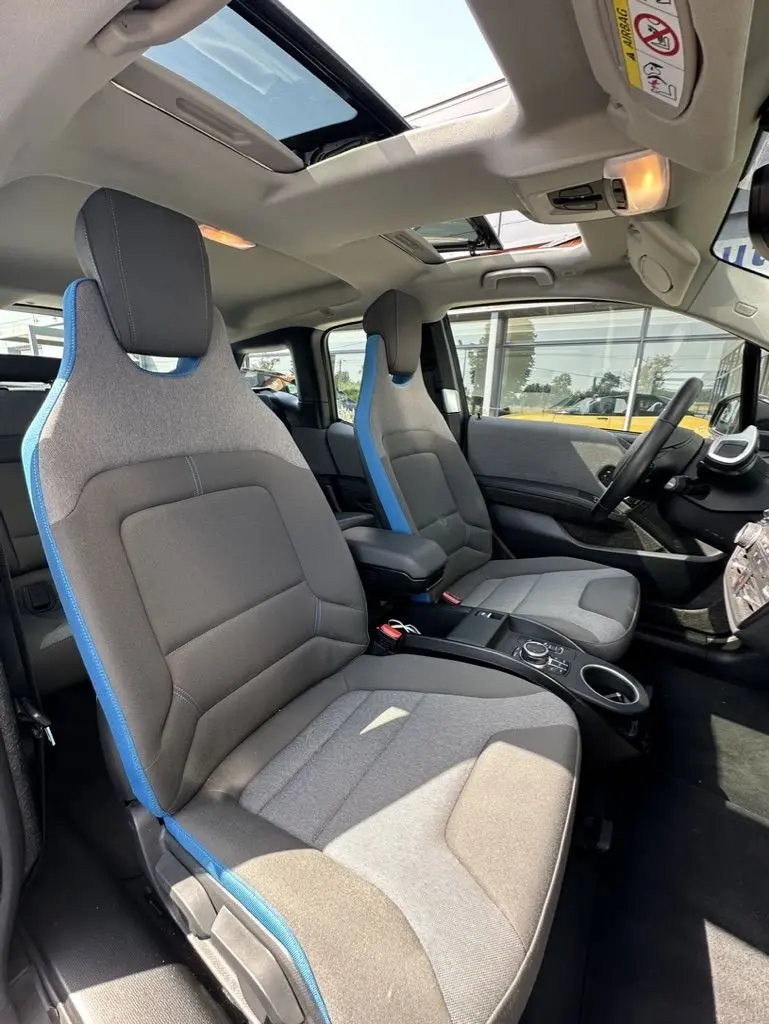 Intérieur de la BMW i3 2022 noir, vue côté droit sur les sièges avant gris avec surpiqûres bleues et toit ouvrant.