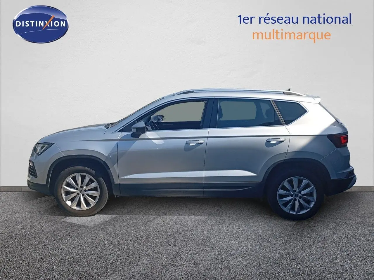 Vue de profil côté gauche d'un SEAT Ateca 2023 argent Reflex Metal avec jantes alliage et toit équipé de barres longitudinales.