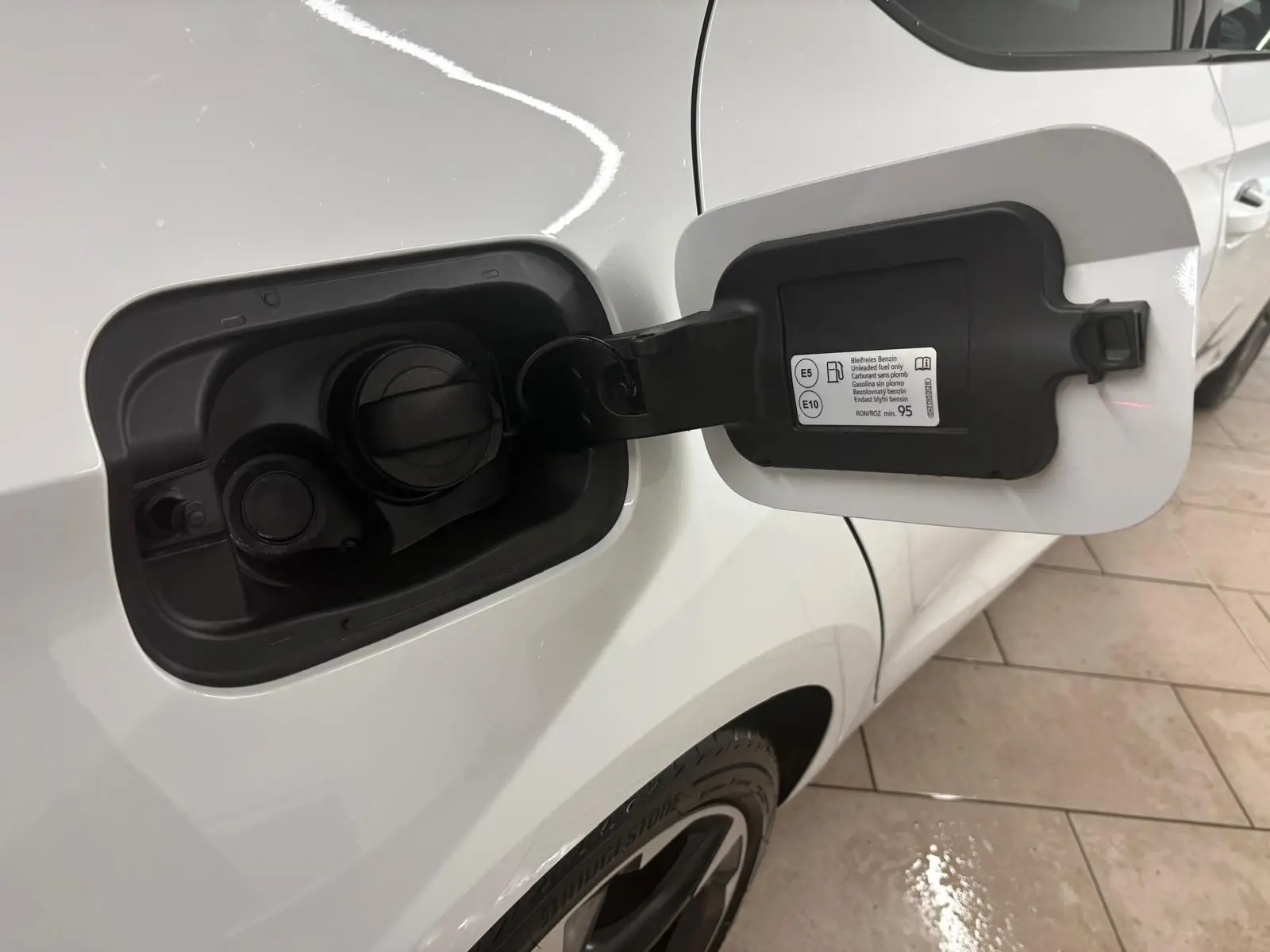 Ouverture de la trappe à carburant côté gauche d'une CUPRA Leon blanc Nevada, vue rapprochée sur la carrosserie et la roue arrière.