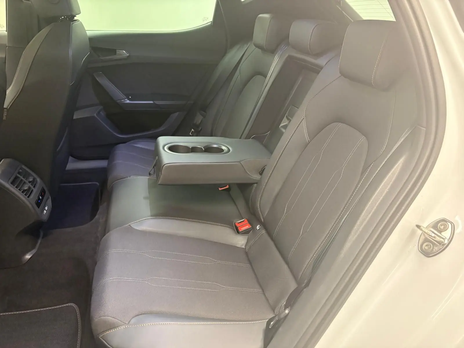 Vue intérieure côté droit des sièges arrière noirs avec accoudoir central et porte ouverte d'une CUPRA Leon blanche Nevada 2024.