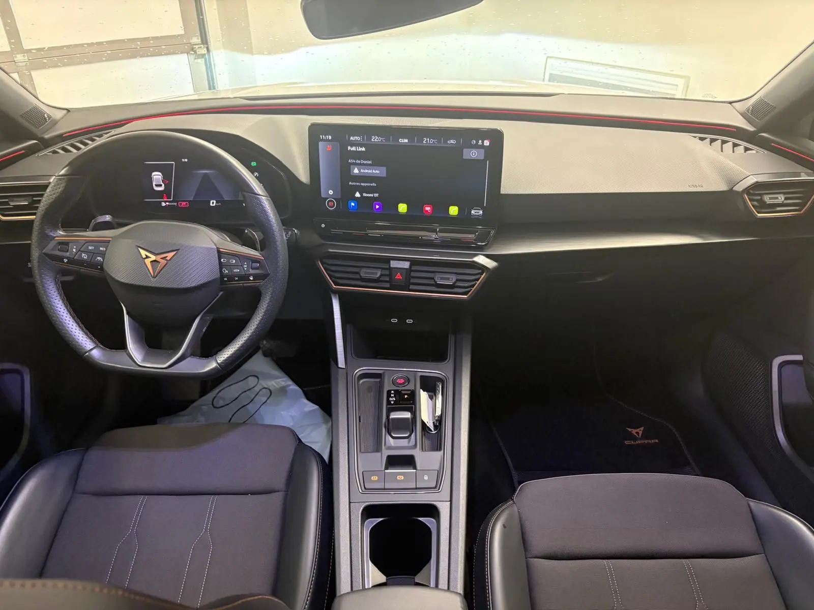 Vue intérieure frontale du tableau de bord et volant noir de la CUPRA Leon 2024 avec écran tactile central allumé.