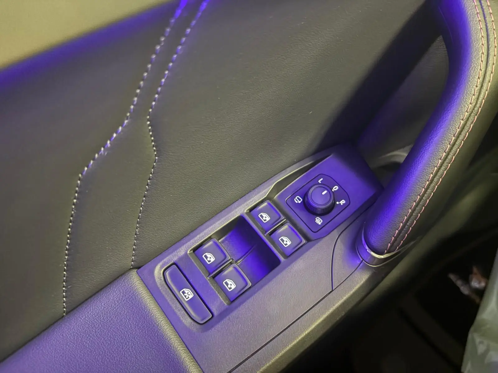 Gros plan sur les commandes des vitres et rétroviseurs côté conducteur, avec surpiqûres rouges sur la garniture noire.
