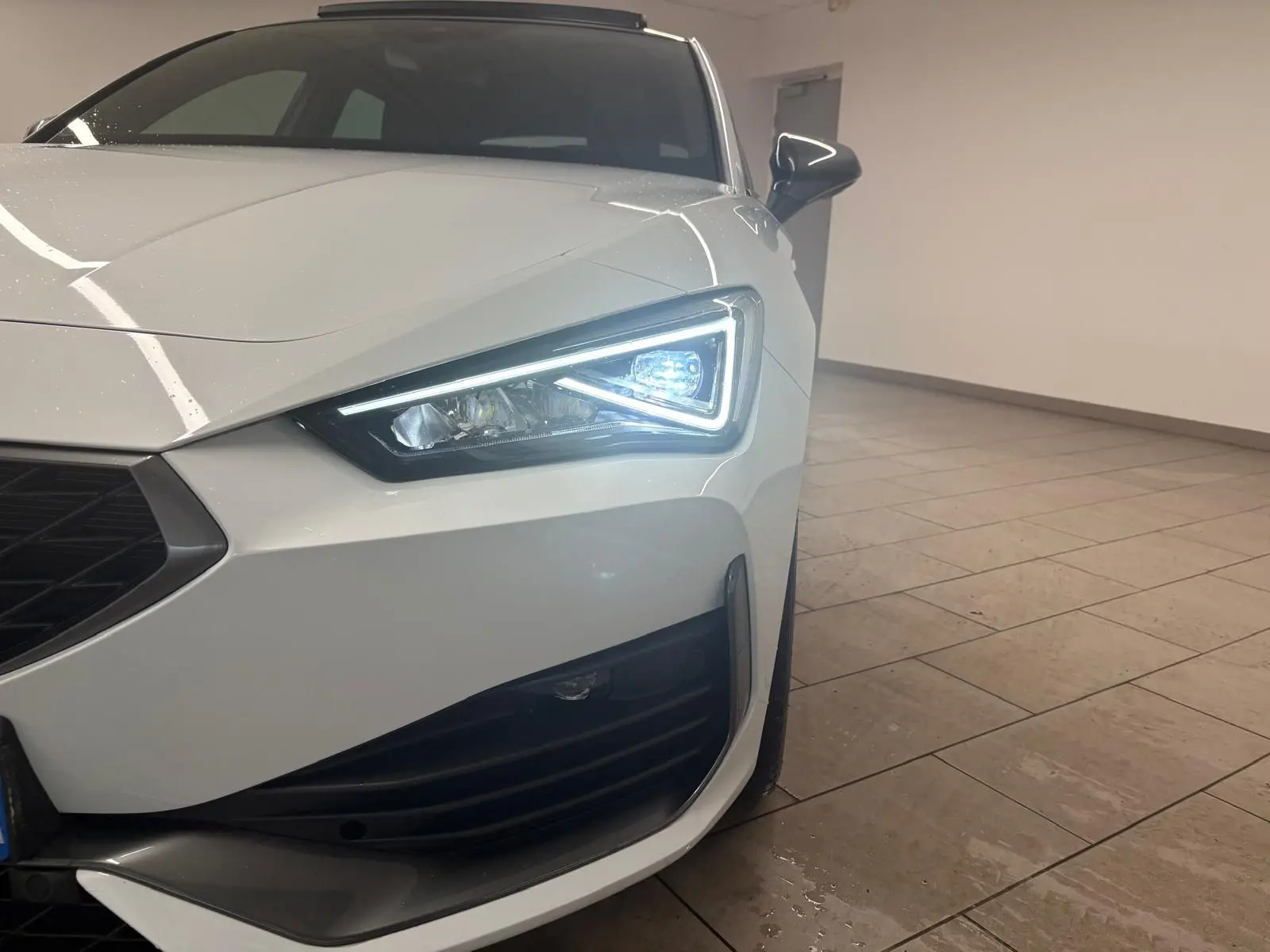 Gros plan sur l'avant droit de la CUPRA Leon blanche Nevada avec phare LED allumé et calandre noire.