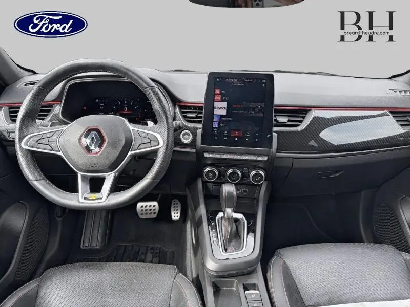 Vue intérieure avant du Renault Arkana 2023 gris métallisé, montrant le volant cuir multifonction et l'écran tactile central vertical.
