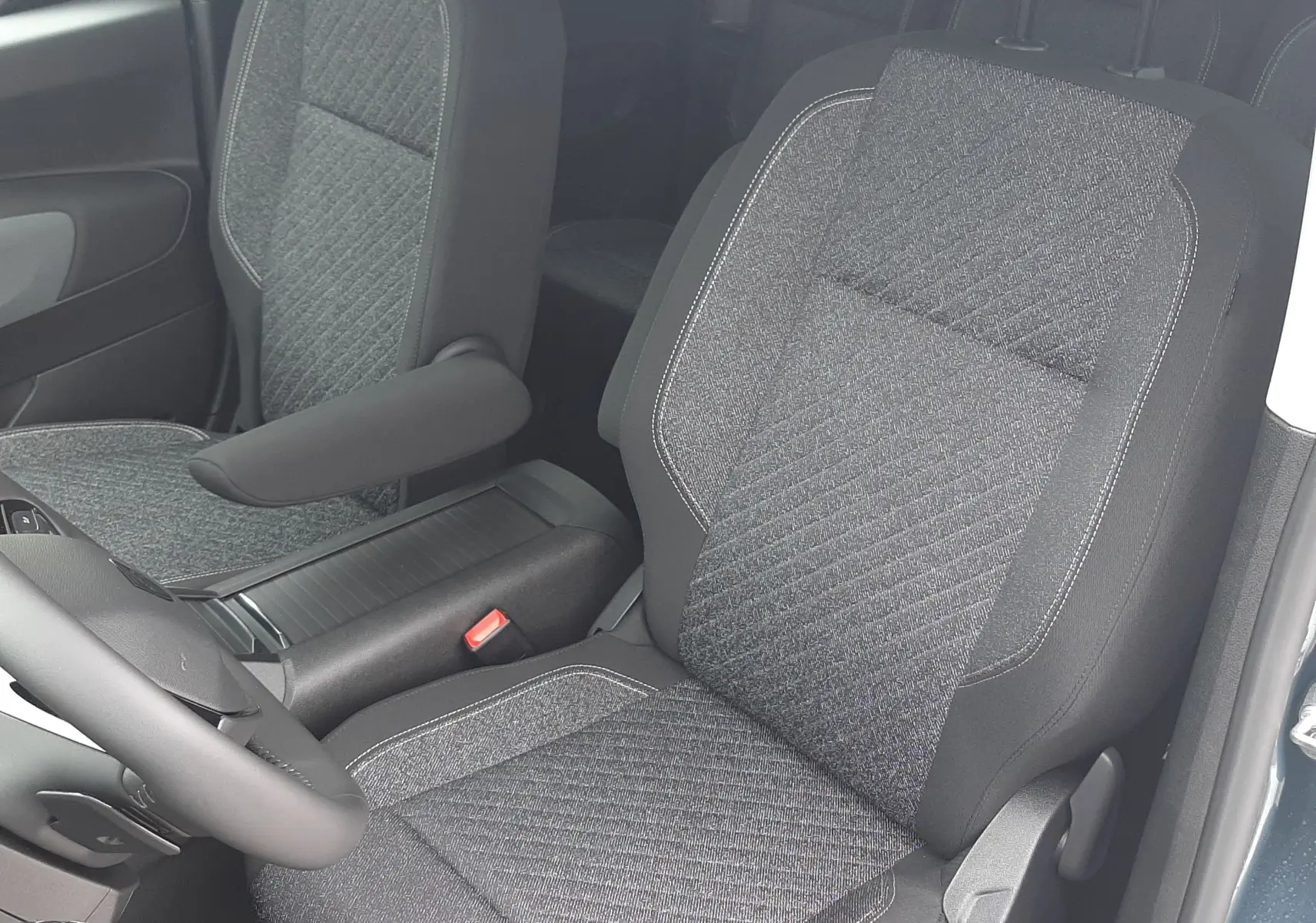 Vue intérieure côté conducteur du Peugeot Rifter 2026, sièges tissu gris avec accoudoir et volant noir visible.