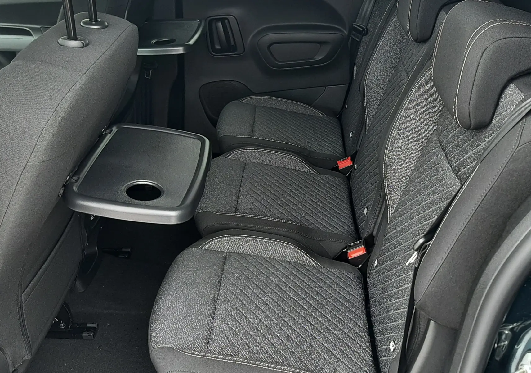 Vue latérale intérieure des sièges arrière gris tissu du Peugeot Rifter 2026, avec tablette rabattable côté gauche.