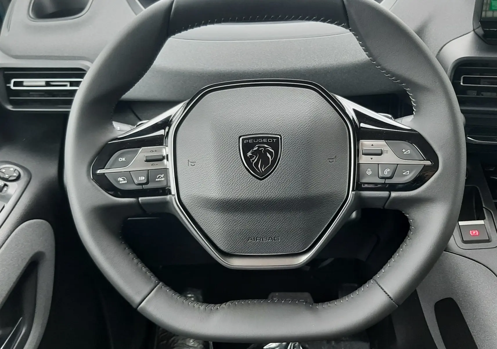 Vue rapprochée du volant noir du Peugeot Rifter 2026 avec commandes intégrées et tableau de bord numérique en arrière-plan.