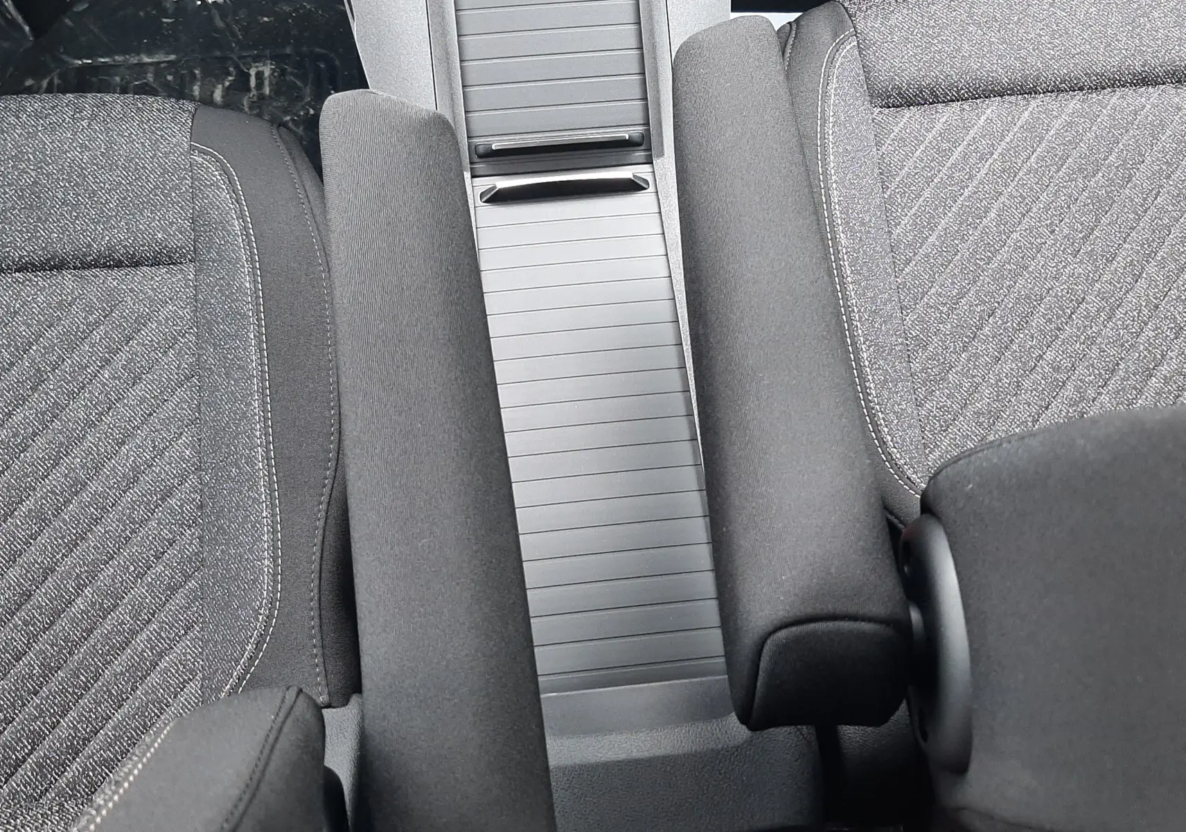 Vue rapprochée de l’intérieur du Peugeot Rifter 2026, montrant la console centrale grise et les accoudoirs noirs entre les sièges tissu gris.