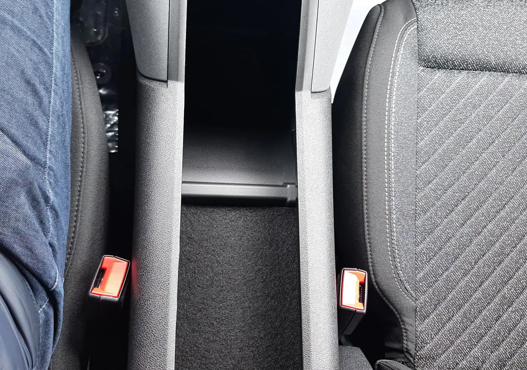 Vue plongeante sur la console centrale et les sièges avant en tissu gris du Peugeot Rifter 2026, intérieur sobre.