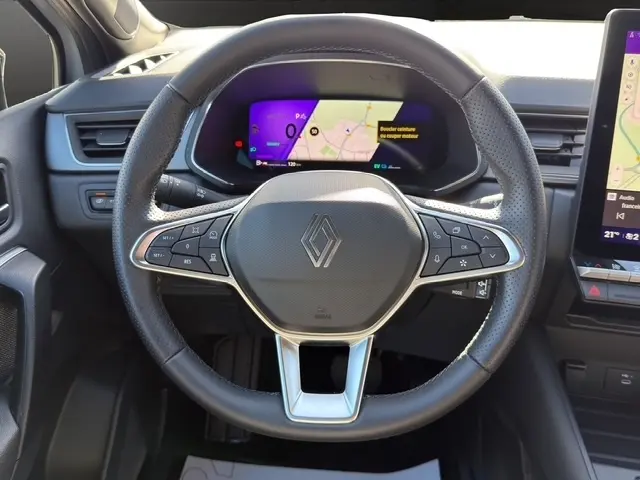Vue rapprochée du volant en cuir synthétique noir du Renault Symbioz 2025 avec tableau de bord numérique coloré en arrière-plan.