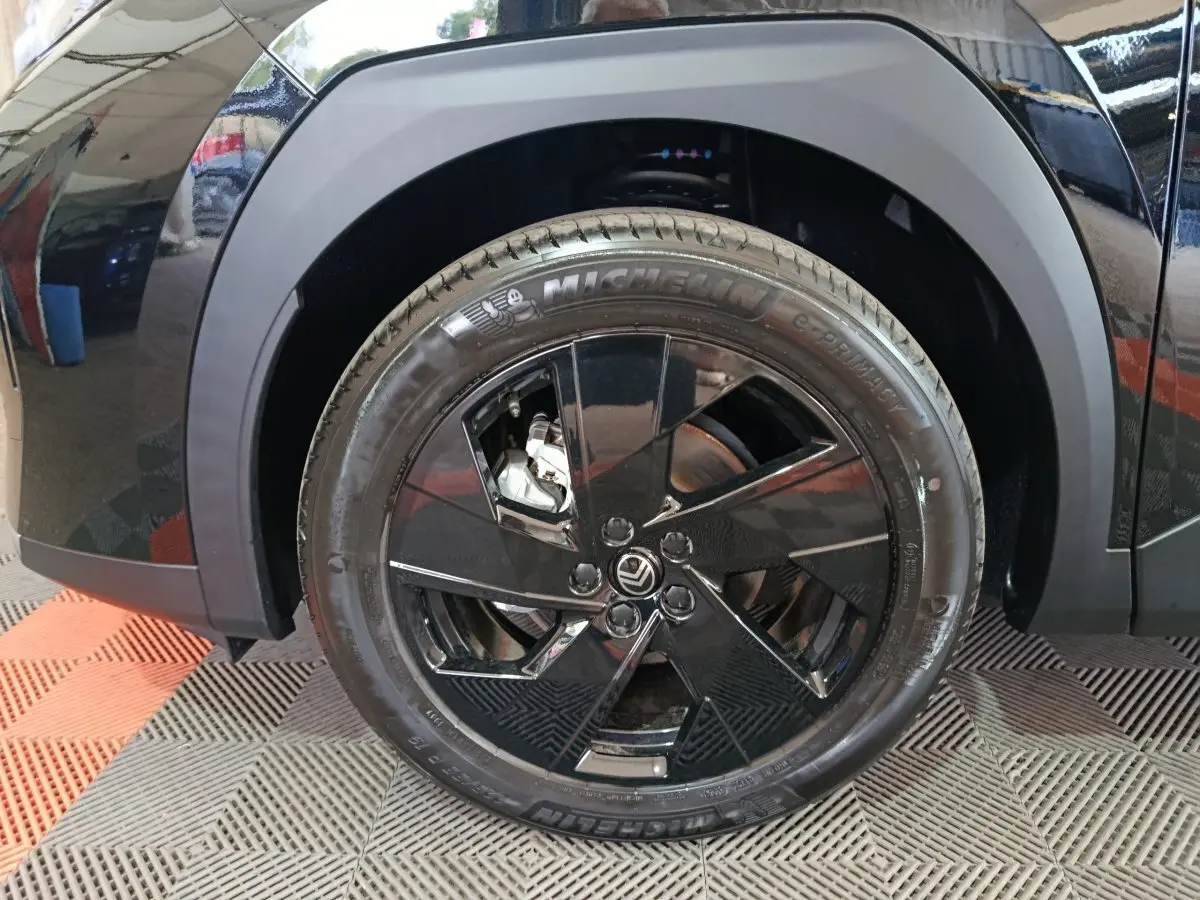 Gros plan sur la roue avant gauche noire avec jante noire brillante et logo Citroën visible sur une C5 hybride.