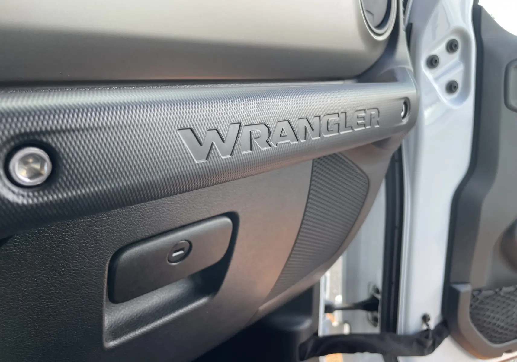 Gros plan sur la poignée intérieure côté passager blanc du Jeep Wrangler 2018 avec logo WRANGLER en relief noir.