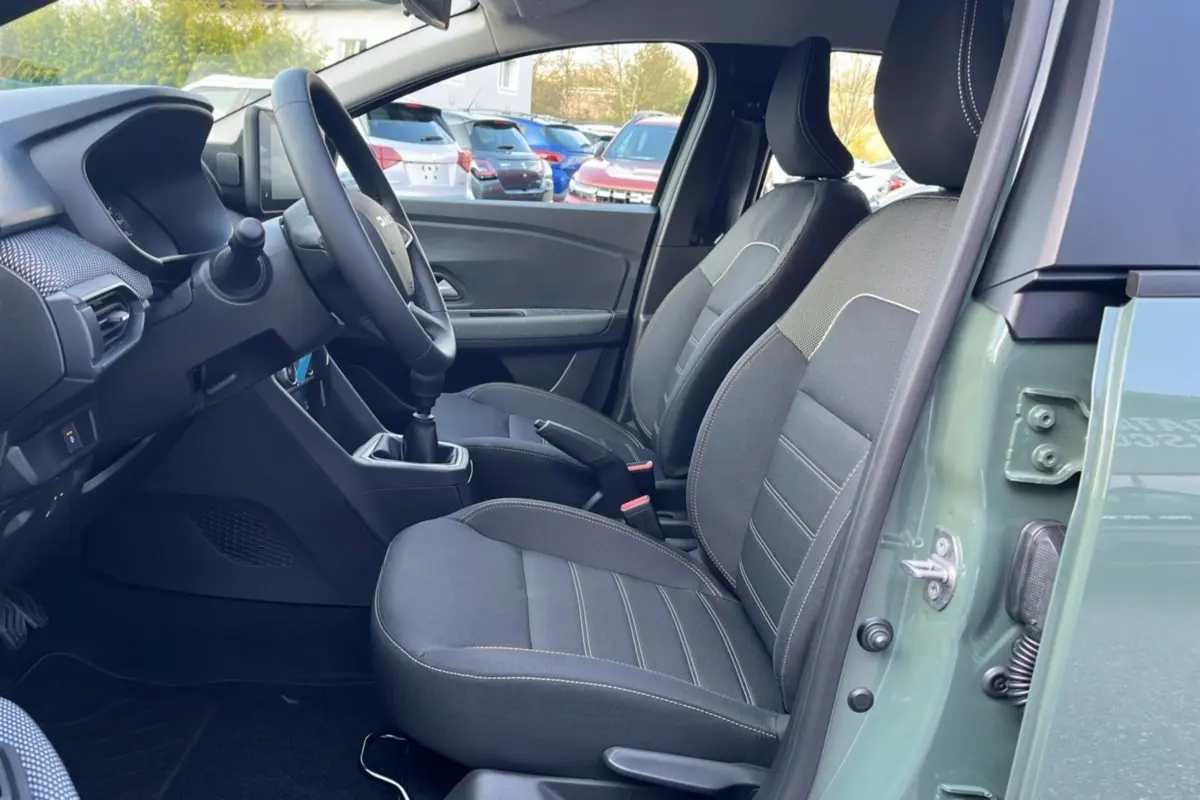Vue intérieure côté conducteur de la Dacia Sandero Stepway 2025 en kaki lichen, avec sièges tissu gris et boîte manuelle.