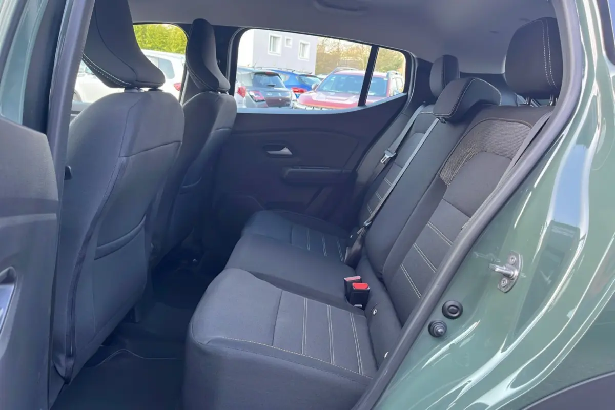 Vue côté droit de l'habitacle arrière d'une Dacia Sandero Stepway 2025 kaki lichen avec sièges en tissu noir et surpiqûres claires.