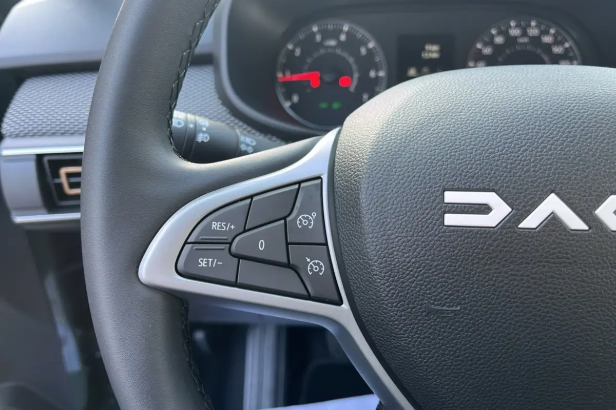 Gros plan sur le volant noir de la Dacia Sandero Stepway 2025 avec commandes de régulateur de vitesse à gauche.