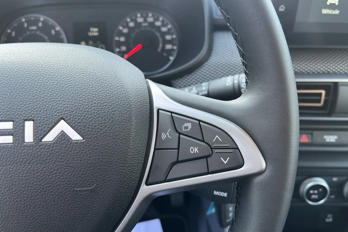 Gros plan sur le volant de la Dacia Sandero Stepway 2025, montrant les commandes multifonctions côté droit en intérieur noir.