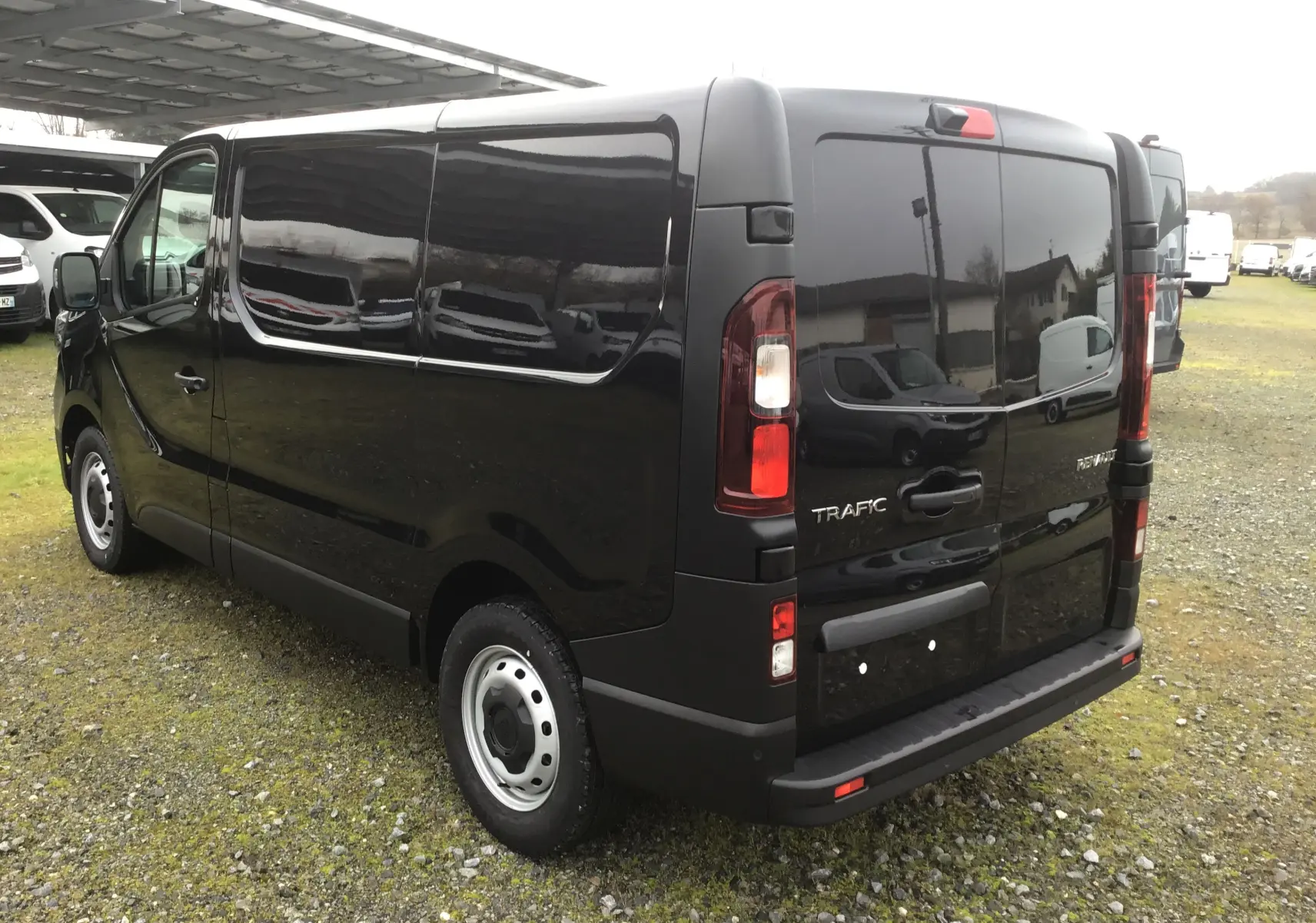 Vue 3/4 arrière droite d’un Renault Trafic Fourgon noir 2025 avec vitres arrière teintées et feux LED.