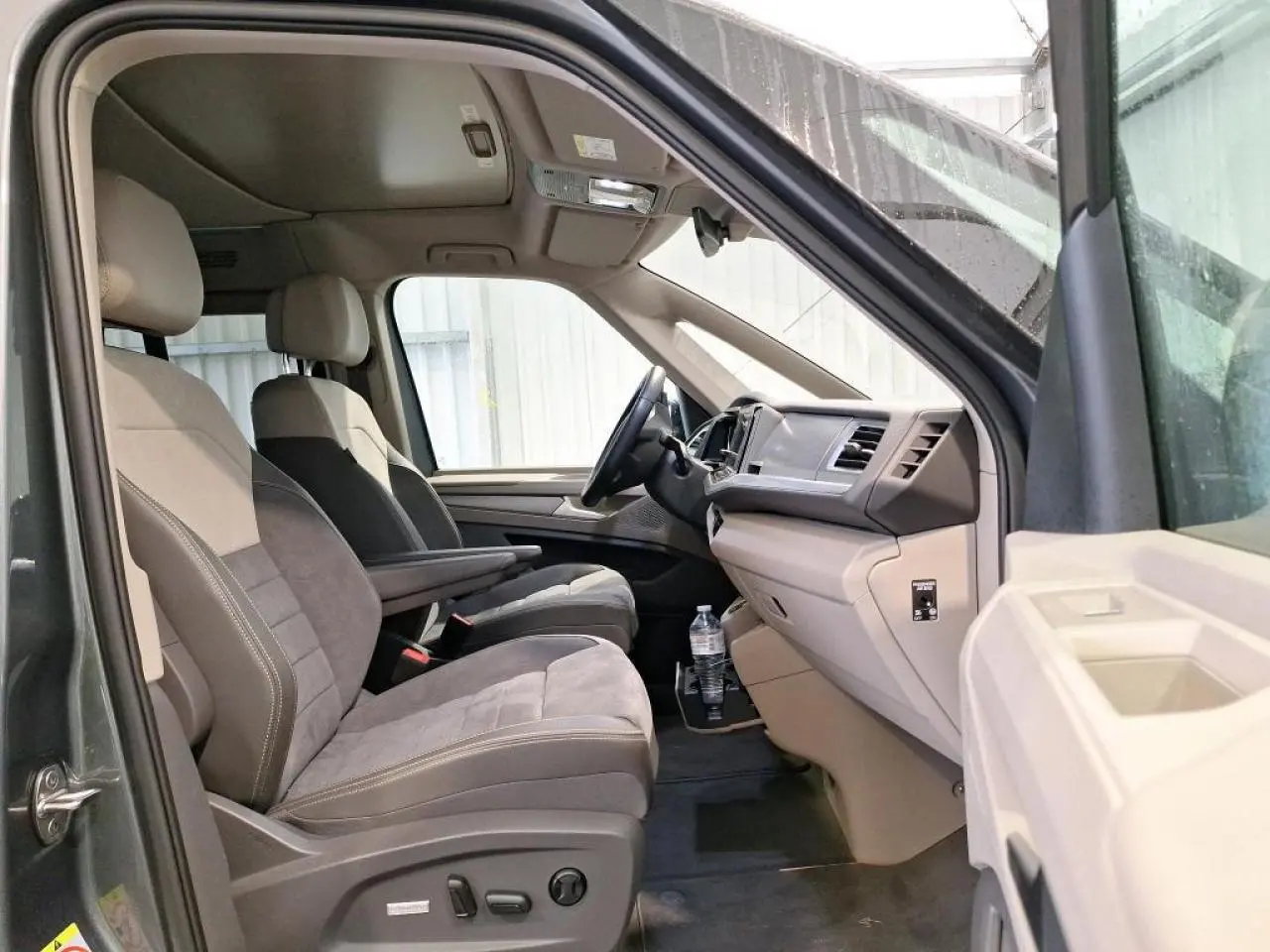 Intérieur côté conducteur du Volkswagen California T7 gris Indium, sièges ErgoComfort bicolores avec accoudoirs et tableau de bord clair.