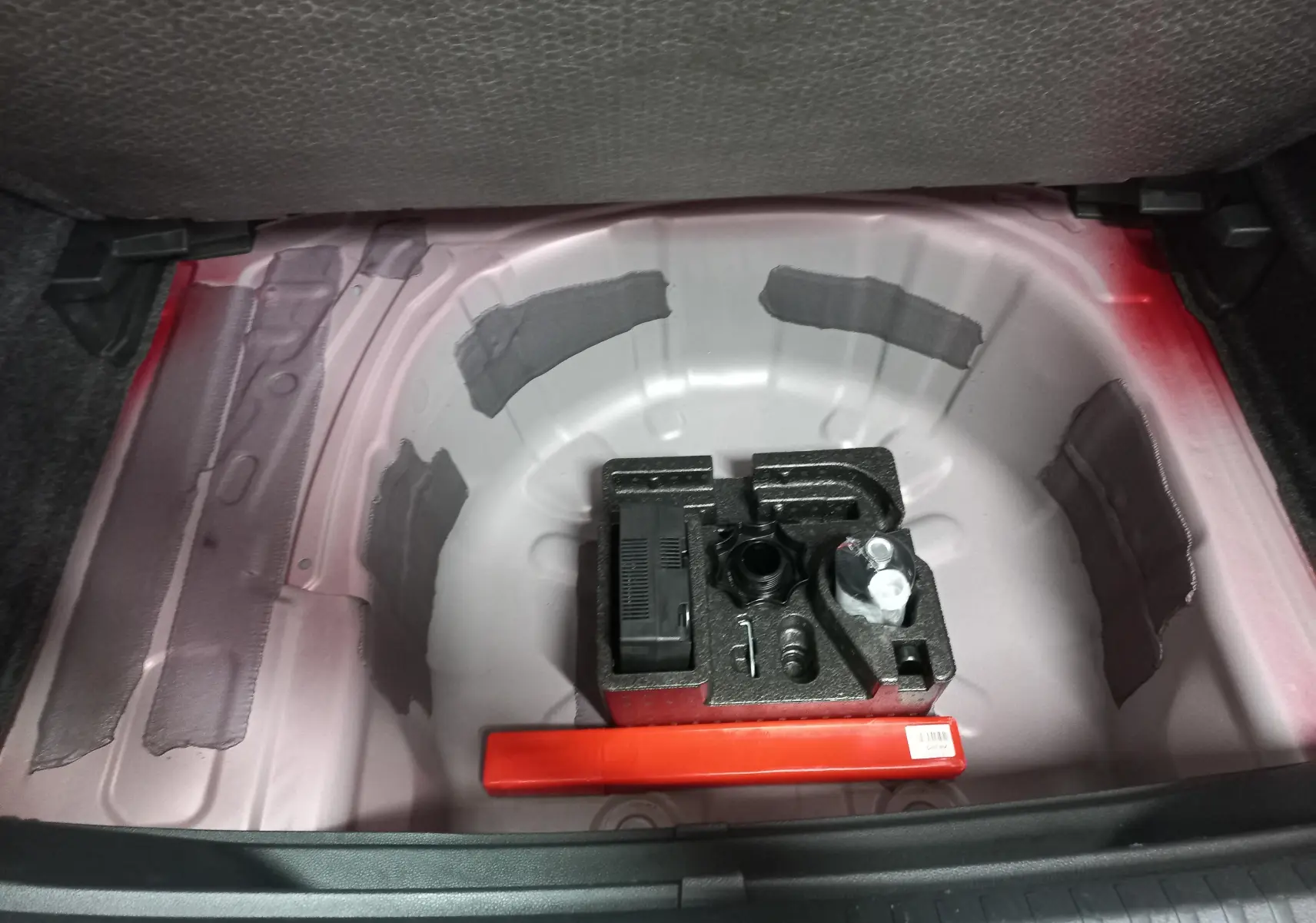 Coffre ouvert montrant la zone de rangement sous plancher avec outils et peinture rouge Désir visible sur la carrosserie.