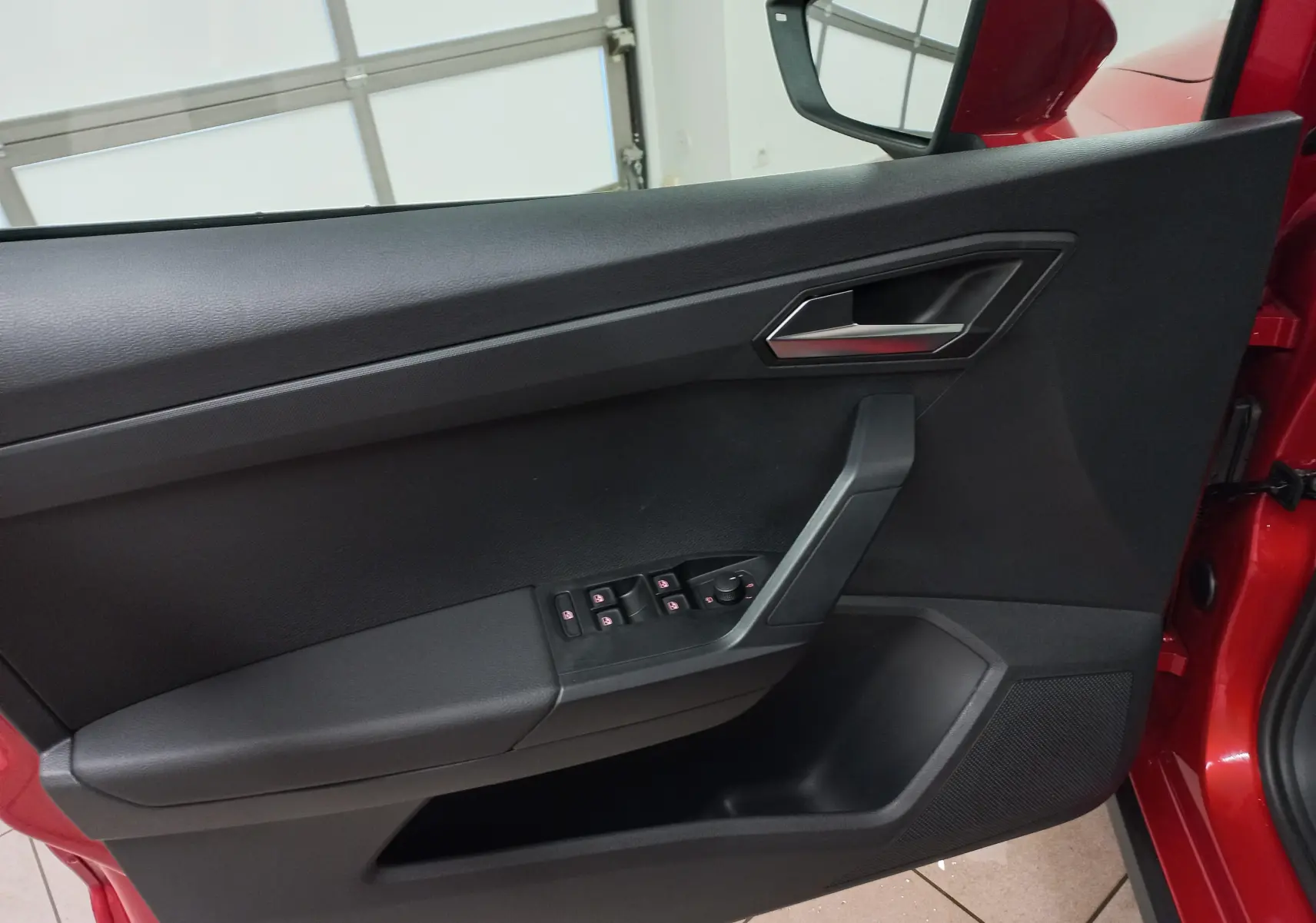 Vue intérieure côté gauche de la porte avant rouge désir avec commandes de vitres et poignée argentée du SEAT Arona 2025.