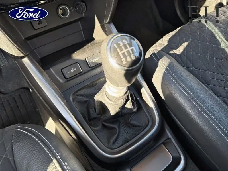 Gros plan intérieur sur le levier de vitesses manuelle et l'accoudoir en cuir noir avec surpiqûres blanches.