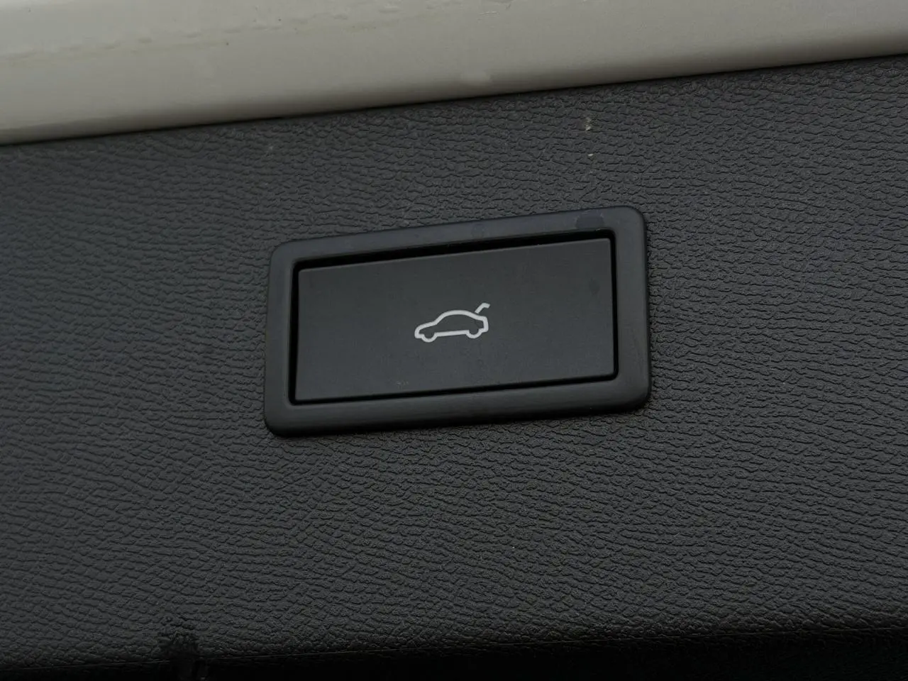 Bouton intérieur noir de commande d'ouverture du hayon du CUPRA Formentor blanc Neige, vue rapprochée sur la texture du panneau.