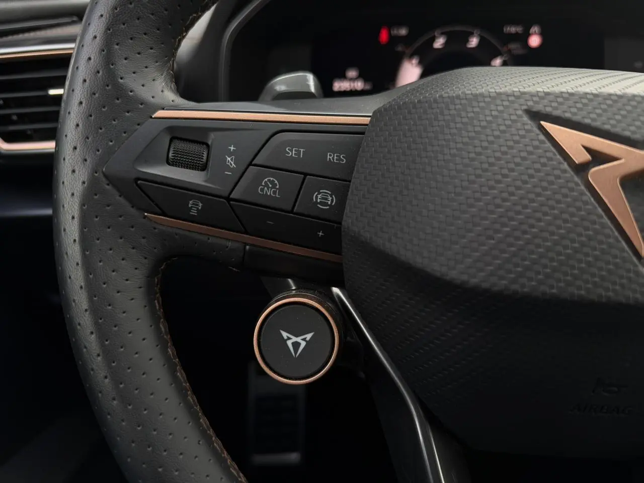 Gros plan sur le volant cuir perforé noir du CUPRA Formentor avec commandes intégrées et logo cuivre distinctif.