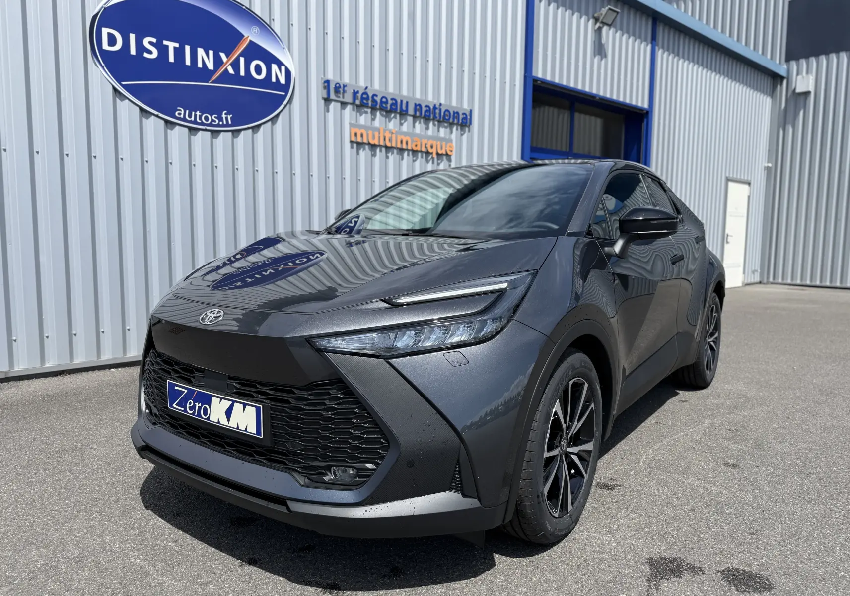 Toyota C-HR 1.8 Hybride gris atlas vu en 3/4 avant droit, avec calandre noire et jantes alliage noires.